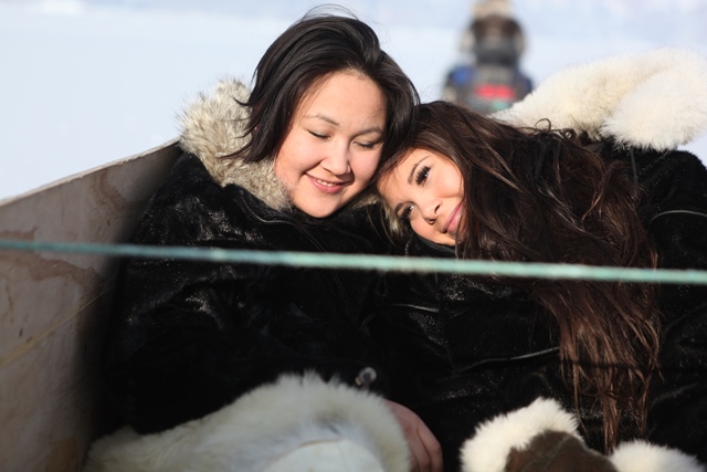 Sara and Pipaluk sitting in the dog sledge box draught by a snowmobile